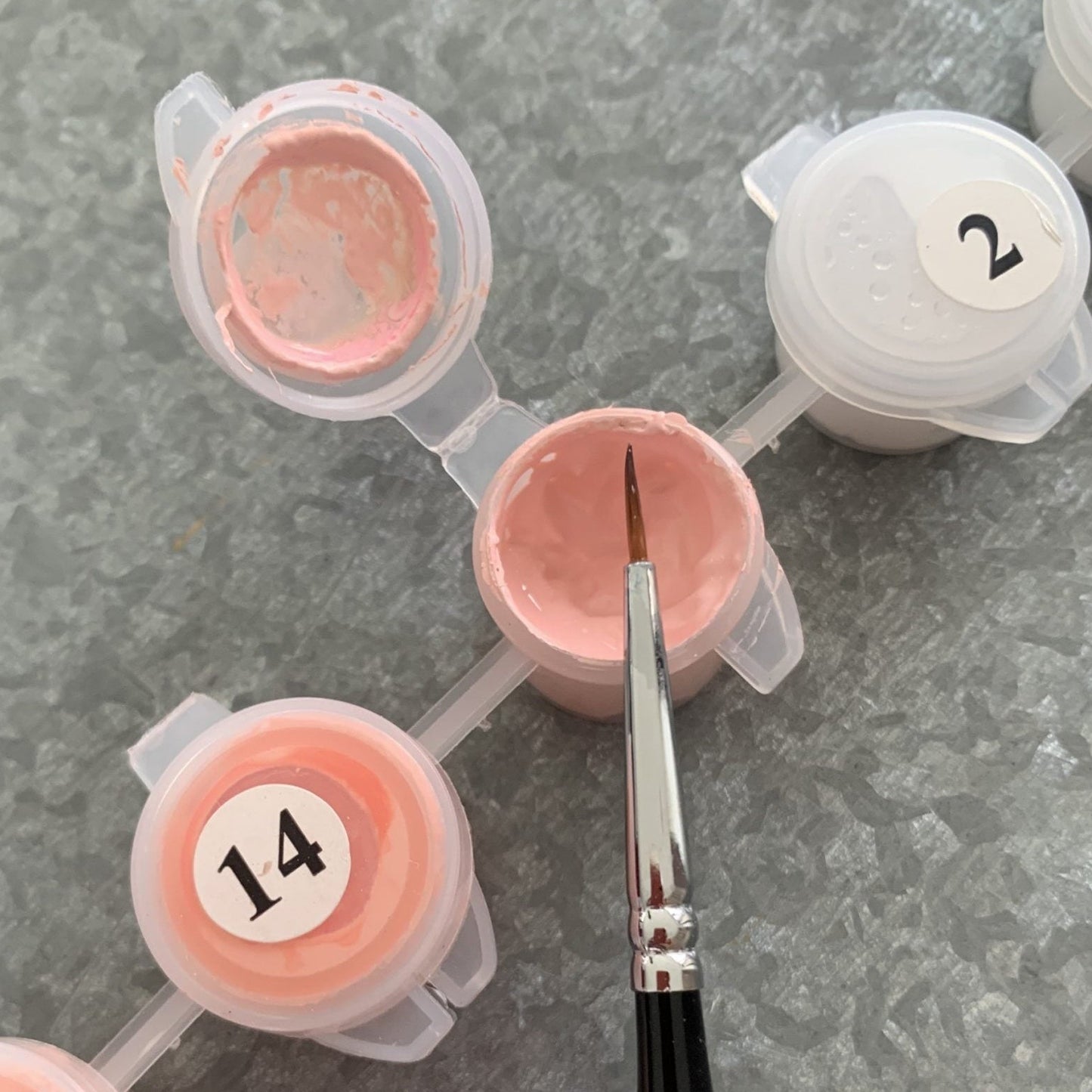 Set of pink paint containers with numbers and a brush on a gray surface