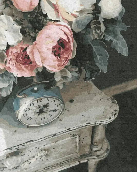 Vintage alarm clock on a wooden surface with pink and white flowers in the background