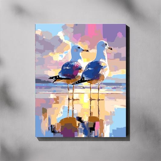 Beach Strolls paint by number kit — completed canvas mockup of two seagulls standing on a wet beach at sunset with a colourful pink, purple and gold sky reflected in the water
