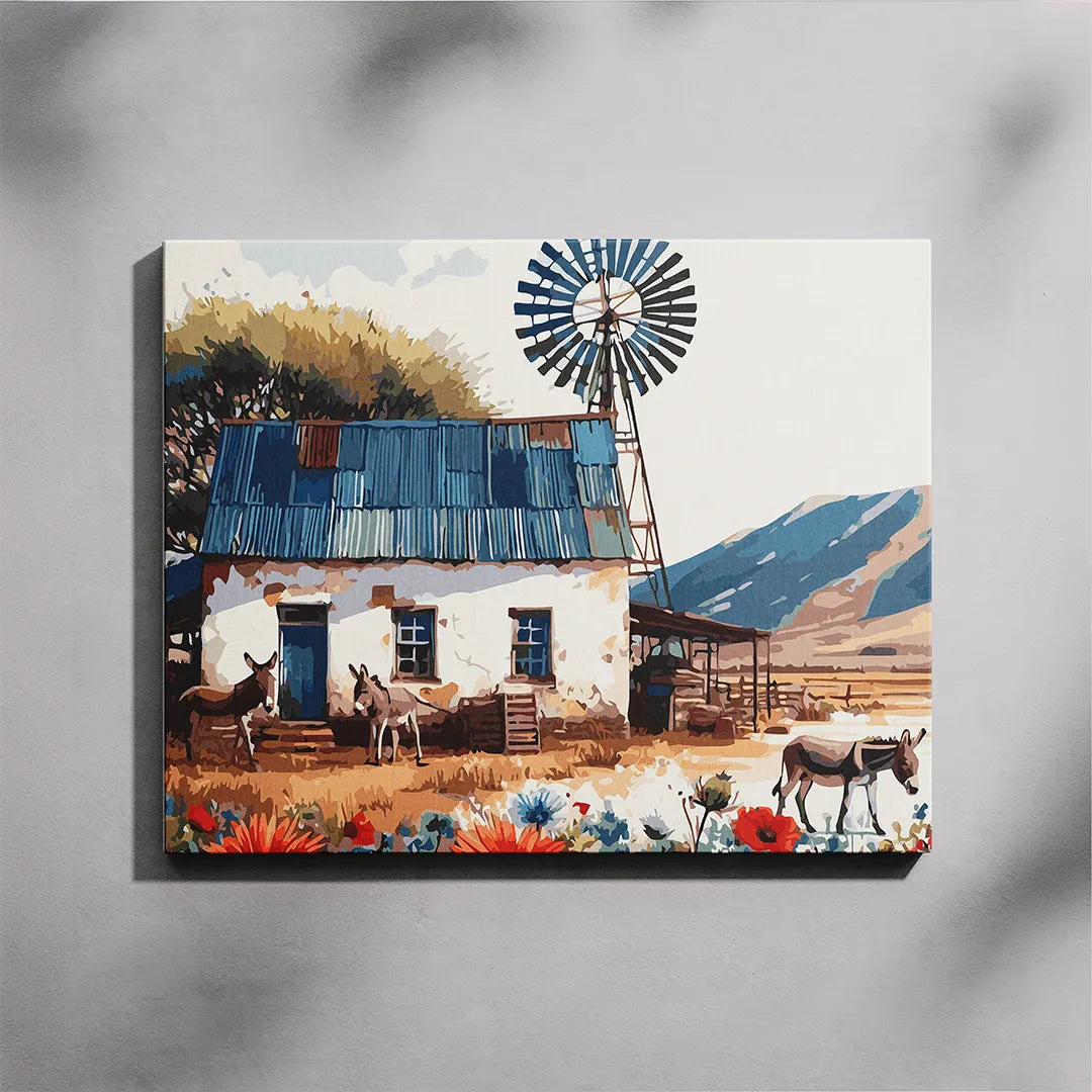 Farm House paint by number kit — completed canvas mockup of a whitewashed Karoo farmhouse with corrugated iron roof, steel windmill, three donkeys and red poppies against blue mountains