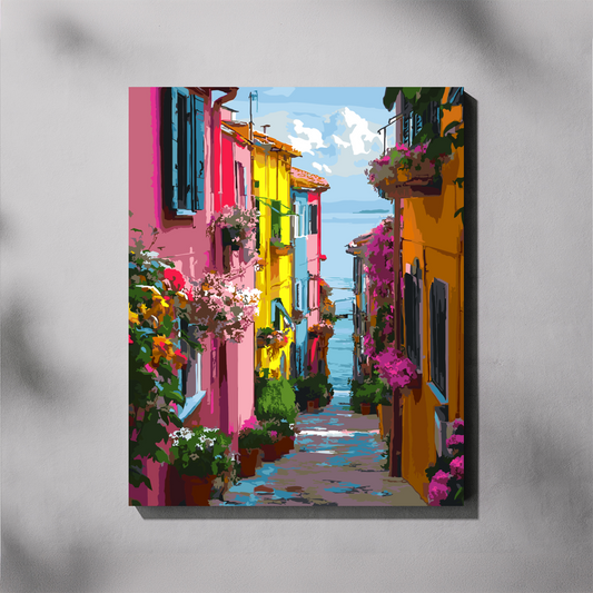 A colorful vertical canvas paint by number of a European village street with vibrant pink, yellow, and orange houses, hanging on a light gray wall.