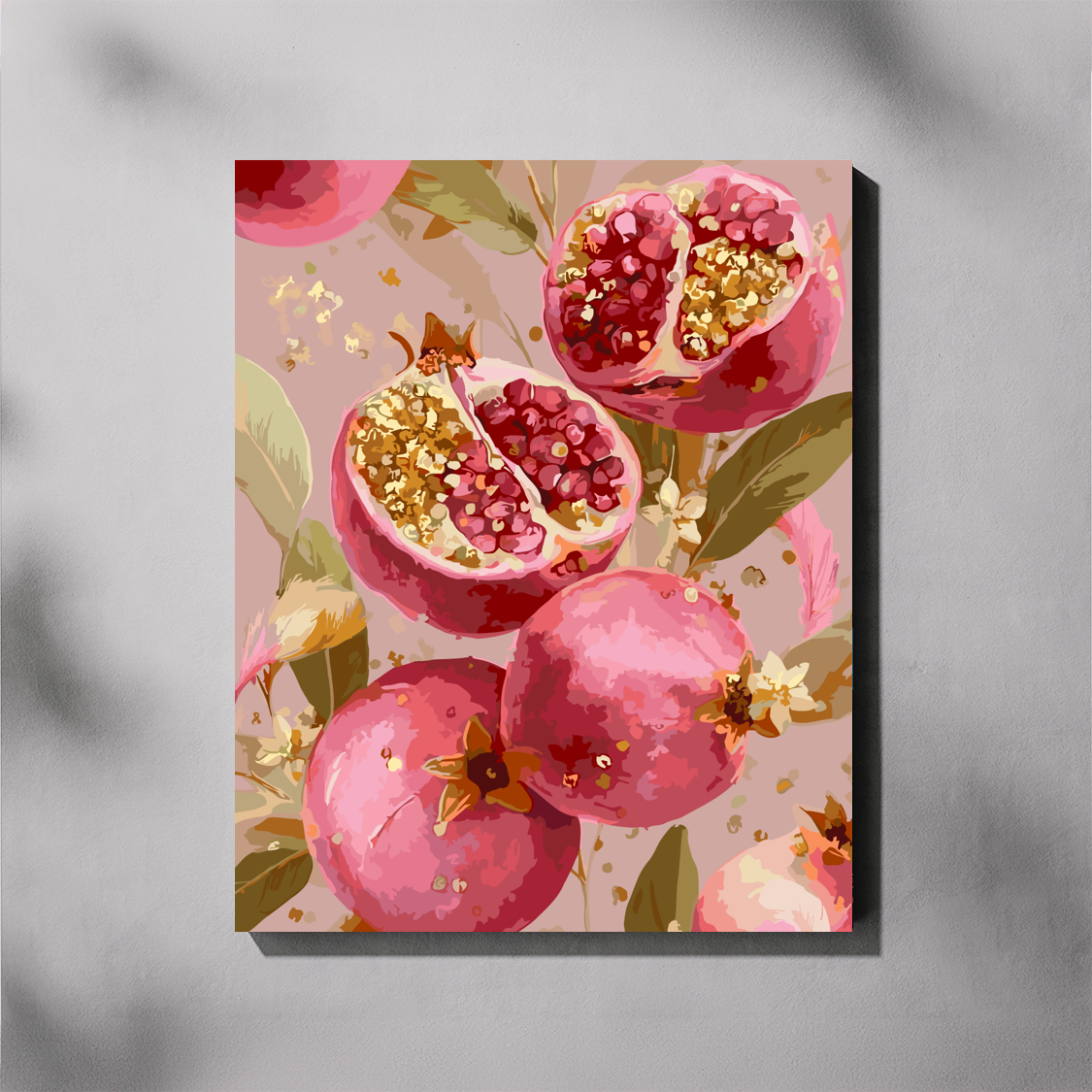 A vertical canvas paint by number featuring a stylized painting of pink pomegranates, some whole and some cut open to reveal red seeds and gold-toned highlights, set against a soft blush background with green leaves. The canvas is shown hanging on a light gray wall with soft shadow overlays.