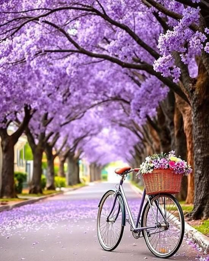 Bicycle with a basket of flowers parked under a canopy of purple flowering trees on a street.