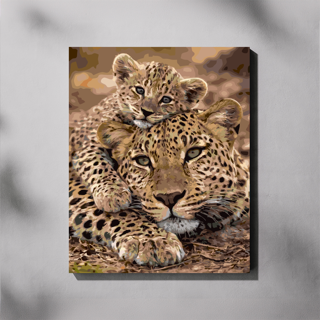 A vertical canvas paint by number depicting a leopard mother and cub resting together, shown hanging on a light gray wall with soft shadow overlays.