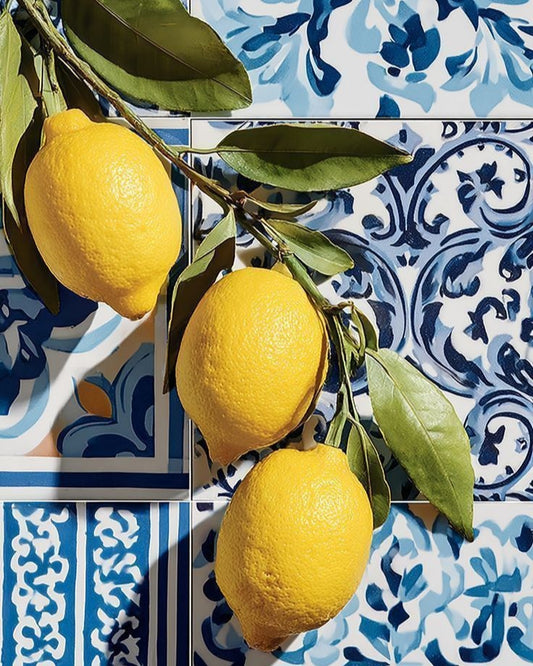 Three lemons on a branch with green leaves against a blue and white patterned tile background