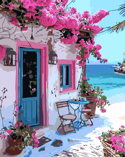 Colorful Mediterranean-style house with pink flowers and a blue door, overlooking the sea.