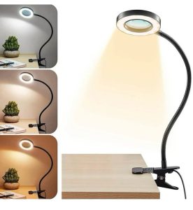 Table lamp with flexible arm on a wooden surface, surrounded by small plants.