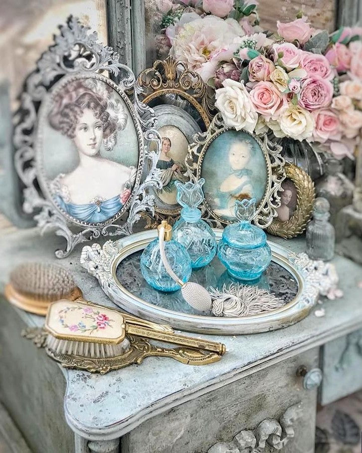 Vintage vanity set with decorative bottles, portraits, and flowers on a distressed wooden surface.