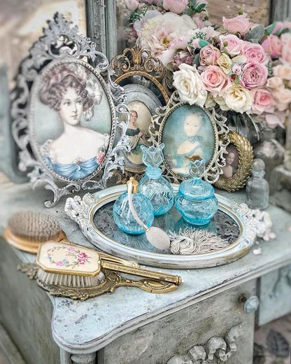 Vintage vanity set with decorative bottles, portraits, and flowers on a distressed wooden surface.