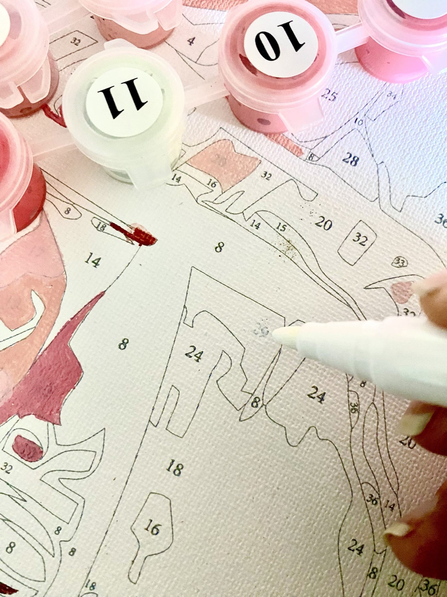 pre-printed canvas with numbers and a pen, surrounded by pink and white paint pots.